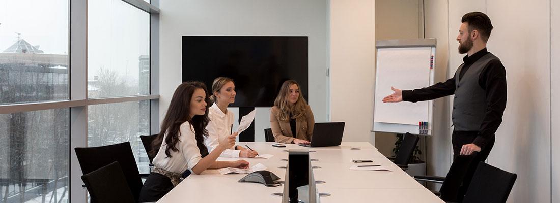 A man is presenting to three women around a large meeting table
